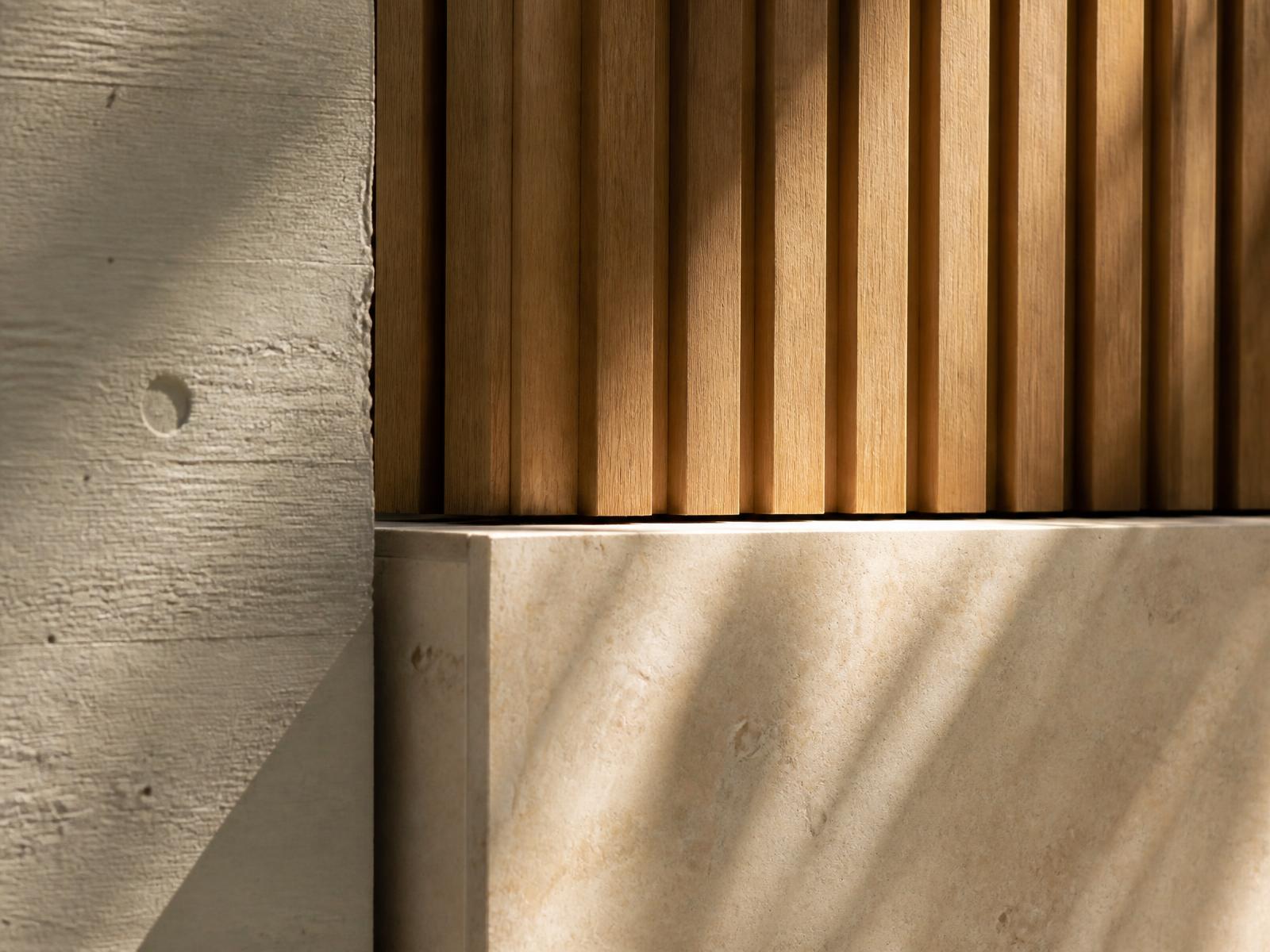 Detail of board-marked concrete, oak slats and limestone in raking sunlight